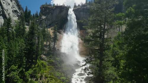 Aerial shot of Yosemite Valley featuring cascading waterfall surrounded by granite cliffs, dense forest, and dramatic mountain landscape in California’s Sierra Nevada.