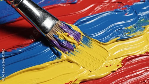 A paintbrush mixes vibrant red, blue and yellow oil paint on a canvas