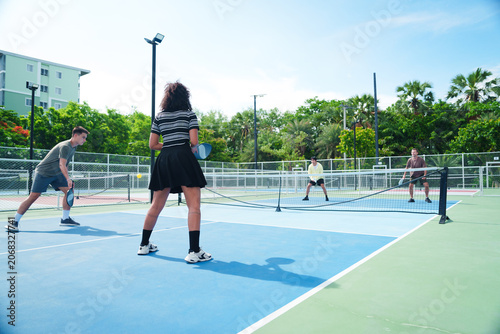 A diverse group of friends in casual athletic playing pickleball together in modern outdoor court. Sports, diversity, active and healthy lifestyle concept
