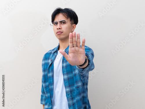 Fotografie Serious young Asian man with glasses showing stop gesture with his palm while st