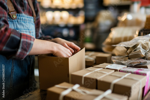 Hands preparing product boxes on table, packaging workflow in shop  