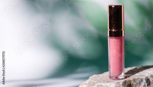 Pink cosmetic gloss displayed on a natural stone slab against a soft blurred green backdrop