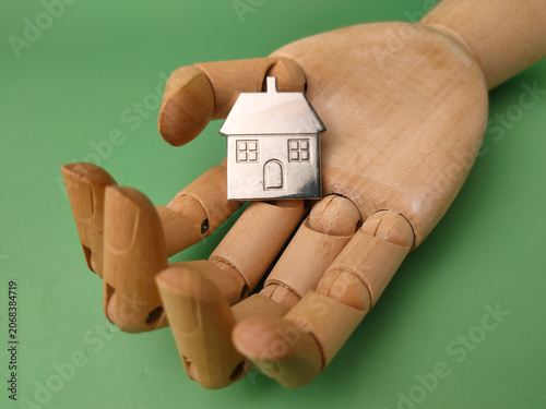 A miniature silver house model rests safely in the open palm of an articulated wooden mannequin hand