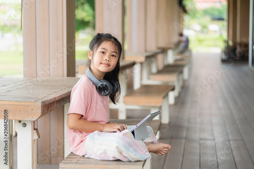 Young Girl Relaxing Outdoors with Digital Tablet and Headphones Sitting on Wooden Bench at a Shelter with Green Scenery in Background