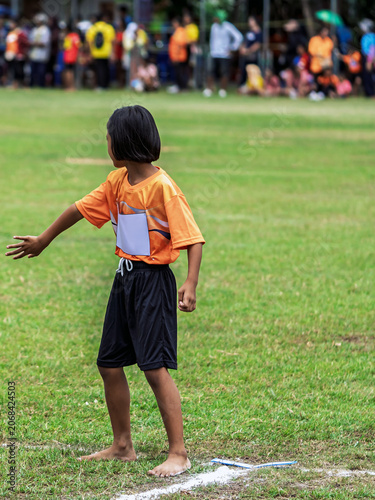 Young schoolgirl standing barefoot on grass running track. Young schoolgirls wearing sports uniforms standing on grass field track while preparing for running competition during sports festival.