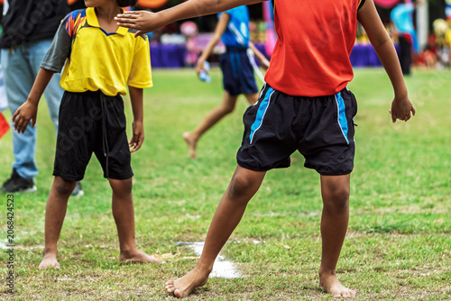 Schoolgirls running barefoot relay race at sports day. Young schoolgirls competing in relay race on grass field, Running barefoot and holding colorful batons during an outdoor school sports festival.
