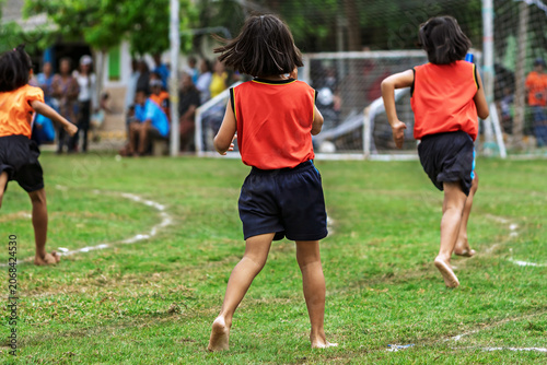 Schoolgirls running barefoot relay race at sports day. Young schoolgirls competing in relay race on grass field, Running barefoot and holding colorful batons during an outdoor school sports festival.