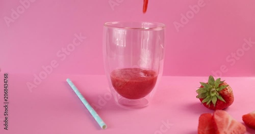 Pouring fresh strawberry smoothie into double walled glass on bright pink background. Healthy summer beverage concept includes organic red berries on colorful surface. Action dynamic shot emphasizes