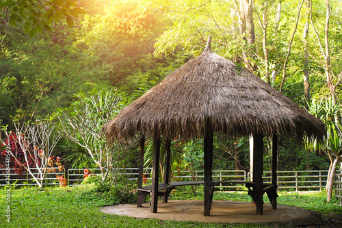 Rustic thatched roof gazebo in a lush green garden with warm sunlight.