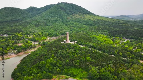 Aerial view of monument tower on forested hill beside river and green mountains