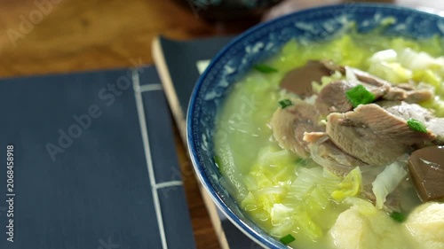 Traditional Asian cabbage noodle soup with meat and tofu in ceramic bowl