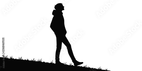 Tableau sur toile Black silhouette of a young man walking up a grassy hill while looking up at the