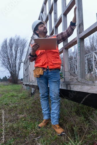 supervisor inspecting a wooden building frame with a digital tablet
