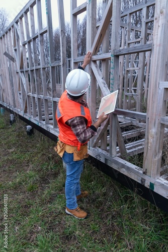 Construction worker inspecting a wooden house frame using a digital tablet on-site