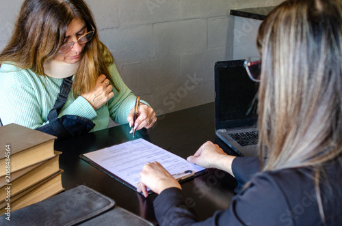 Schilderij op canvas Injured woman signing an insurance claim or legal contract with lawyer