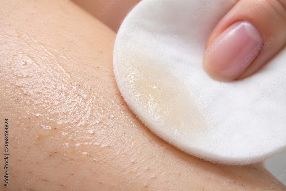 Fototapeta premium Woman applying cosmetic lotion with cotton pad on leg after hair removal session. Skincare routine for smooth skin. Procedure for body care, dermatological treatment and epilation concept.