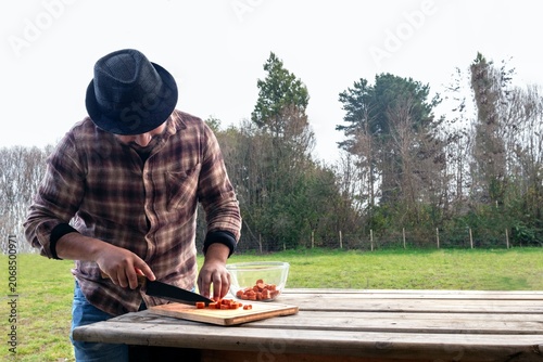 Man chopping sausages on a wooden cutting board outdoors in a rural setting