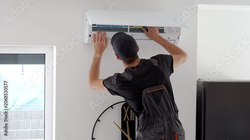 Man servicing an open wall air conditioner checking the filter panel. Concept of AC repair maintenance and cooling system service.