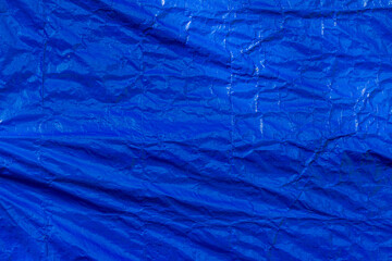 A bright dark blue polyethylene tarp with signs of stretching and creasing. A fine rectangular weave pattern is visible.