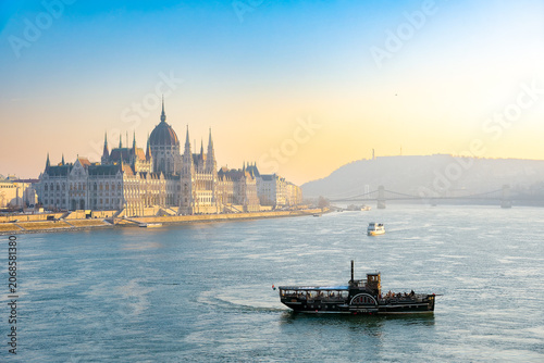 Vintage-style paddle steamboat cruise on the Danube River with the Hungarian Parliament Building at sunrise in Budapest, Hungary