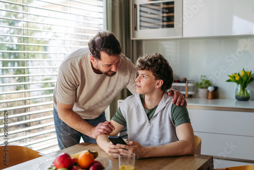 Father supporting teenage son at home during everyday moment.
