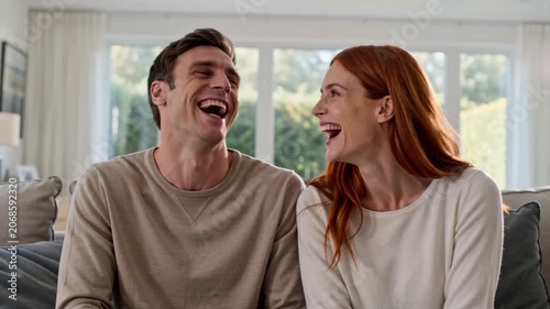 Happy Couple Laughing Together While Sitting on Sofa at Home