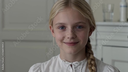 Portrait of a young blonde girl smiling at the camera indoors