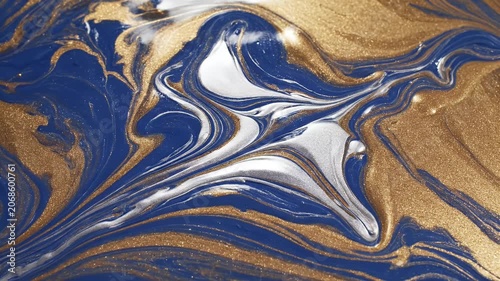 A close-up shot showcases swirling patterns of blue and gold paint being manipulated by a dark tool, creating an abstract and mesmerizing artistic effect.