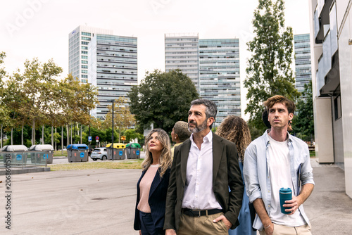 Billede på lærred Group of diverse business people walking on an urban street, looking up at moder