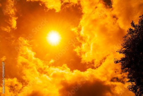 Dramatic blazing sun shining through fiery orange clouds during an extreme heatwave, global boiling and climate crisis concept, hot summer weather background.
