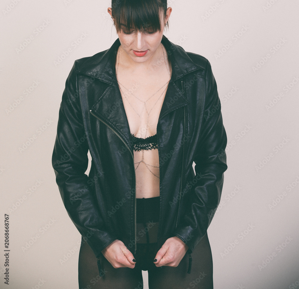 Naklejka premium Frau mit Lederjacke und schwarzem Outfit im Studio. Ausdrucksstarkes Fashion-Motiv für Selbstbewusstsein, Urban Style, Rock Chic, Mode und moderne Weiblichkeit.