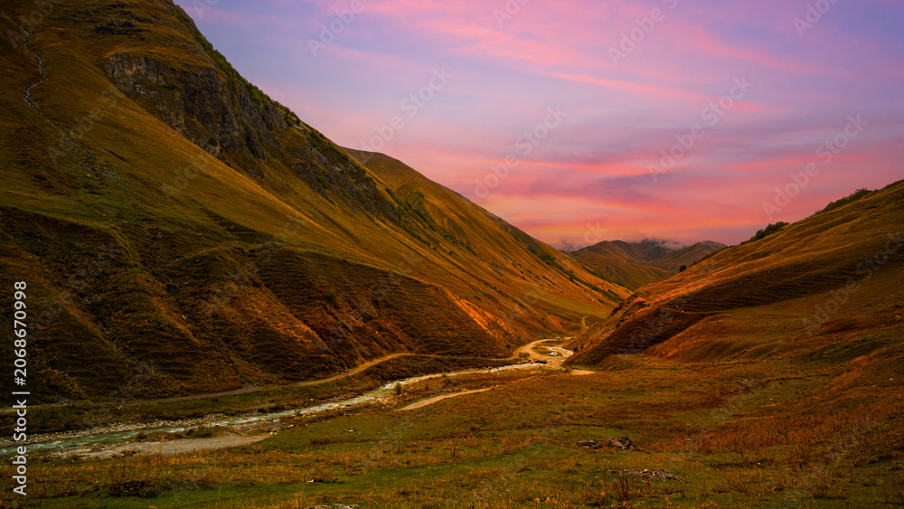 Obraz premium Scenic mountain valley with winding river under a colorful sunset sky