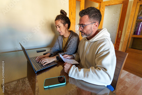 Couple managing home finances, reviewing documents and using laptop for online banking at home