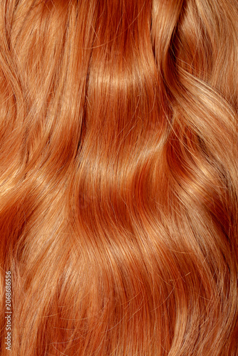Red hair close-up as a background. Women's long orange hair. Beautifully styled wavy shiny curls. Hair coloring bright shades. Hairdressing procedures, extension.