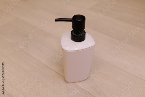A white bottle with a pump is placed on a light wooden floor. It has a simple design