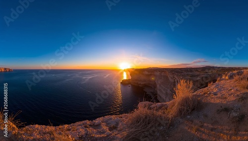Bathing coastal cliff and dry grass on bluff in sunset light, ocean reflecting, copy space