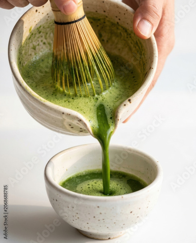 Green tea, bamboo whisk, ceramic bowl, pouring, foam, Japanese tea method with hand mixing powder in cup, warm beverage ritual on light background