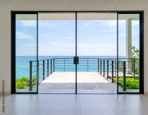 A modern interior showcases expansive glass sliding doors offering a breathtaking view of a turquoise ocean and clear blue sky.