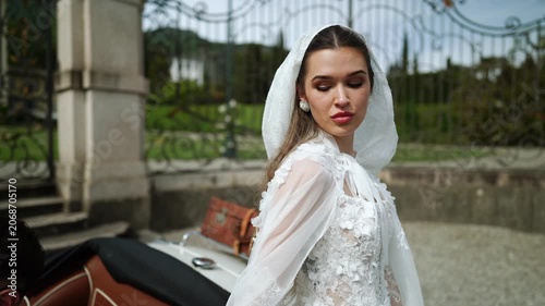 Beautiful woman in white vintage dress stands by classic car at elegant estate