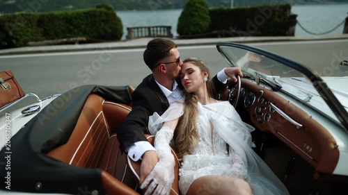 Romantic kiss shared by elegant couple in vintage convertible car by the lake