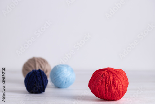 Set of yarn balls in red, light blue, beige and navy blue placed on light gray wooden surface. Horizontal minimalist image with copy space. Concept of knitting supplies and handmade creativity