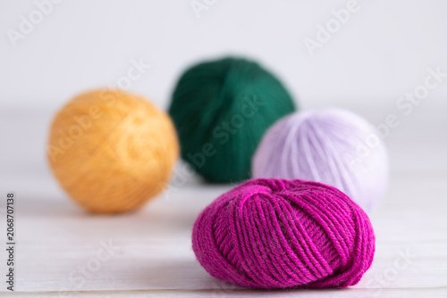 Yarn balls in fuchsia, green, mustard yellow and lilac colors on light gray surface. Colorful horizontal photo with neutral background and copy space