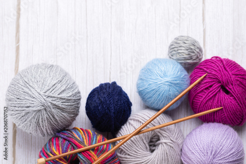 Top view of yarn balls in gray, blue, lilac, fuchsia and multicolor tones with wooden knitting needles on light gray table. Horizontal image with copy space