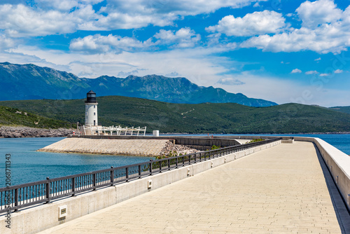 Stately white lighthouse standing watch over the azure waters and stone breakwater of Lustica Bay