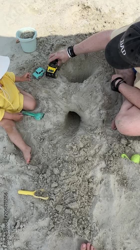 Child and parent building a sand tunnel on the beach