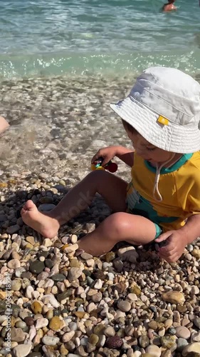 Young child sitting on pebble beach by clear sea