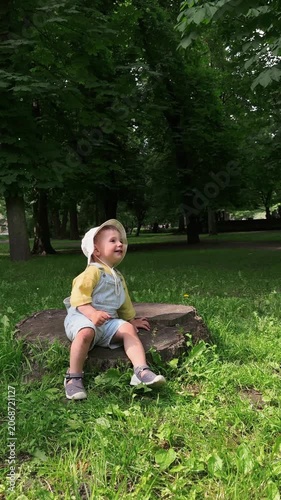 Smiling toddler sitting on tree stump in green park