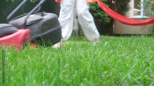 Person mowing backyard lawn near red hammock