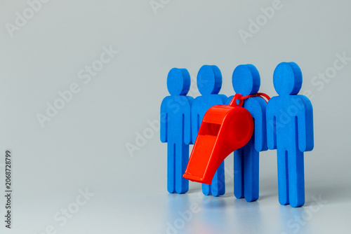 Fotografie A red whistle hanging on a blue figure among a group on a grey background