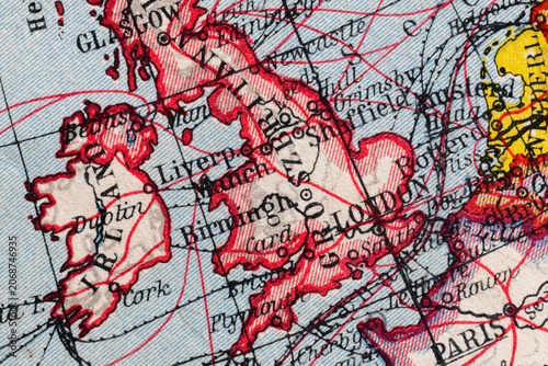 Close-up macro image of a vintage map fragment showing Ireland and Great Britain with route lines, old place names and aged paper texture. Historical cartography background for travel, geography and a